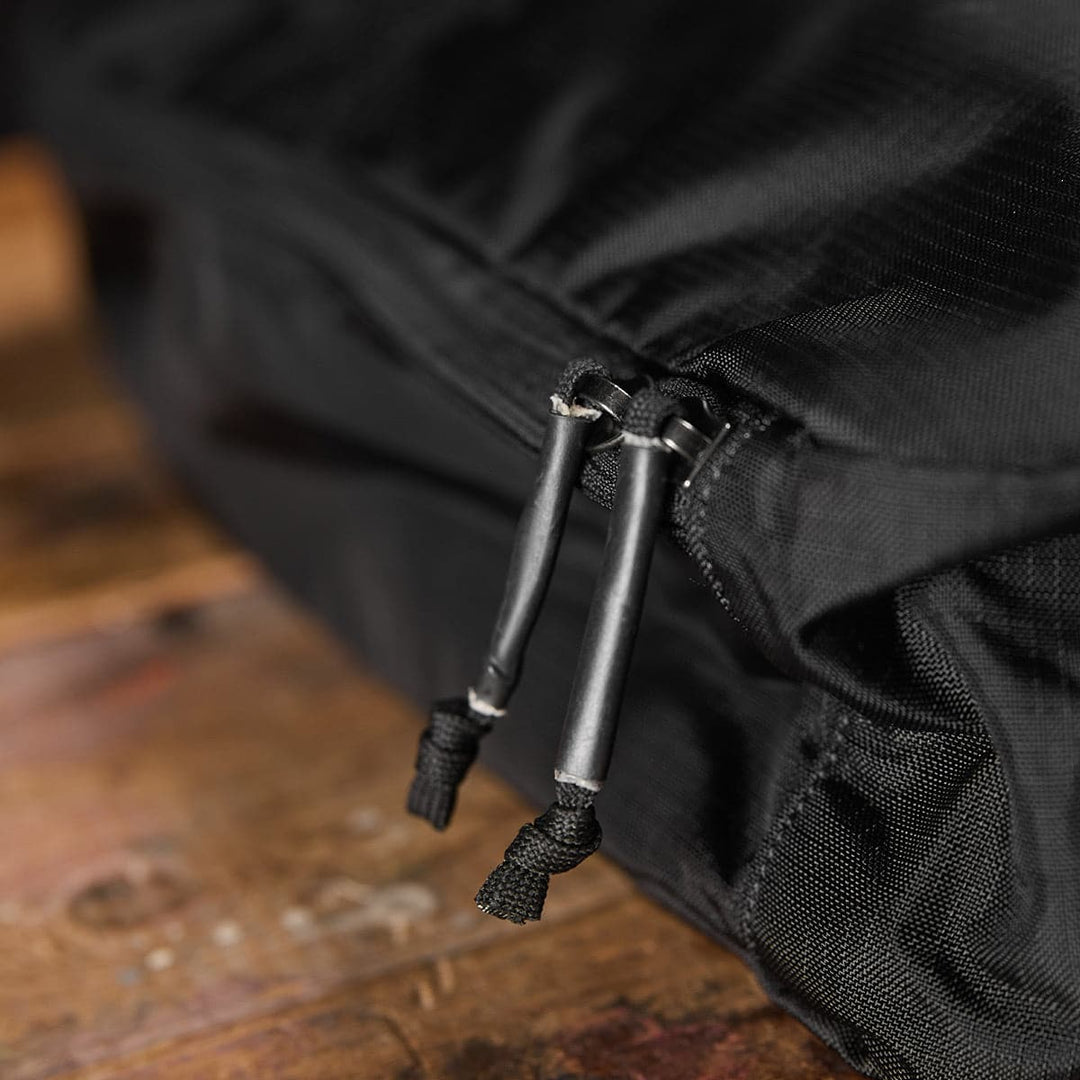 Close-up of a water-resistant zipper with braided pulls on the GORUCK Ripstop ROBIC Shoe Bag, displayed on a wooden surface.