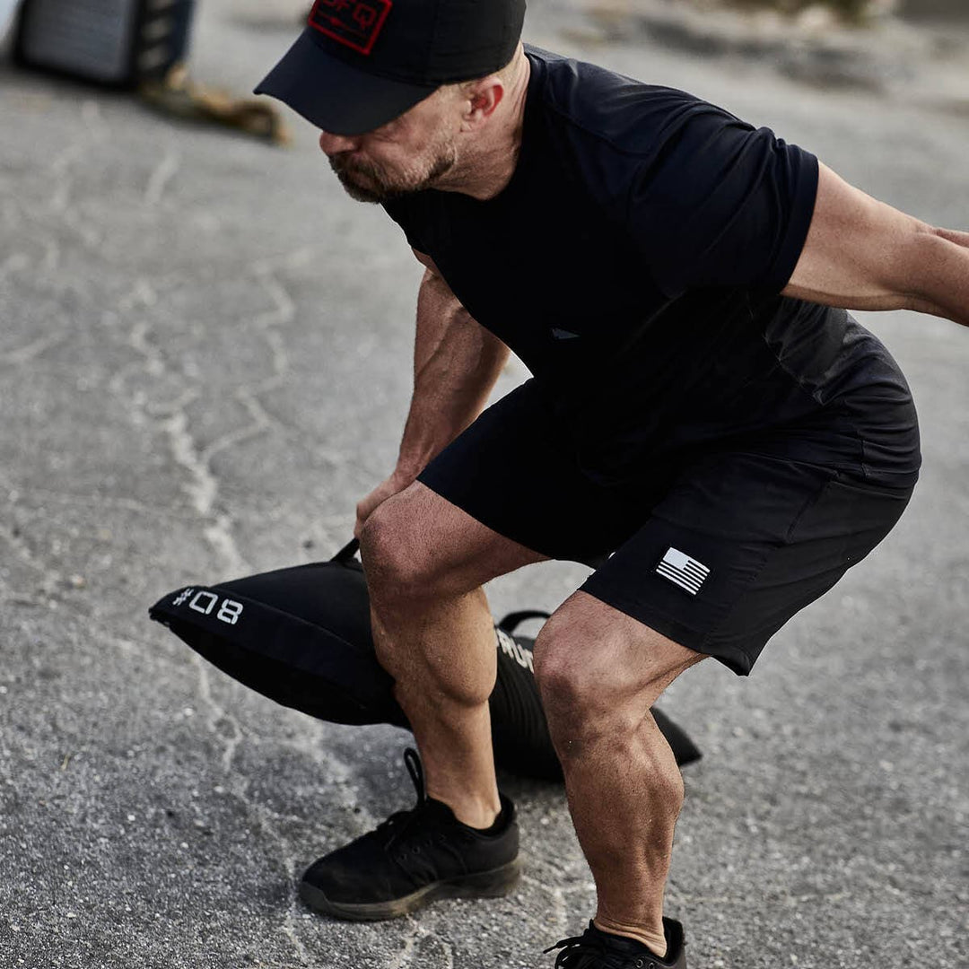 A man in athletic wear is lifting a heavy GORUCK Simple Training Sandbag outdoors, showcasing the versatility often found in home gym setups.