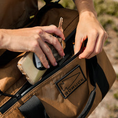 Hand placing keys and wallet into a tan GORUCK rucksack outdoors