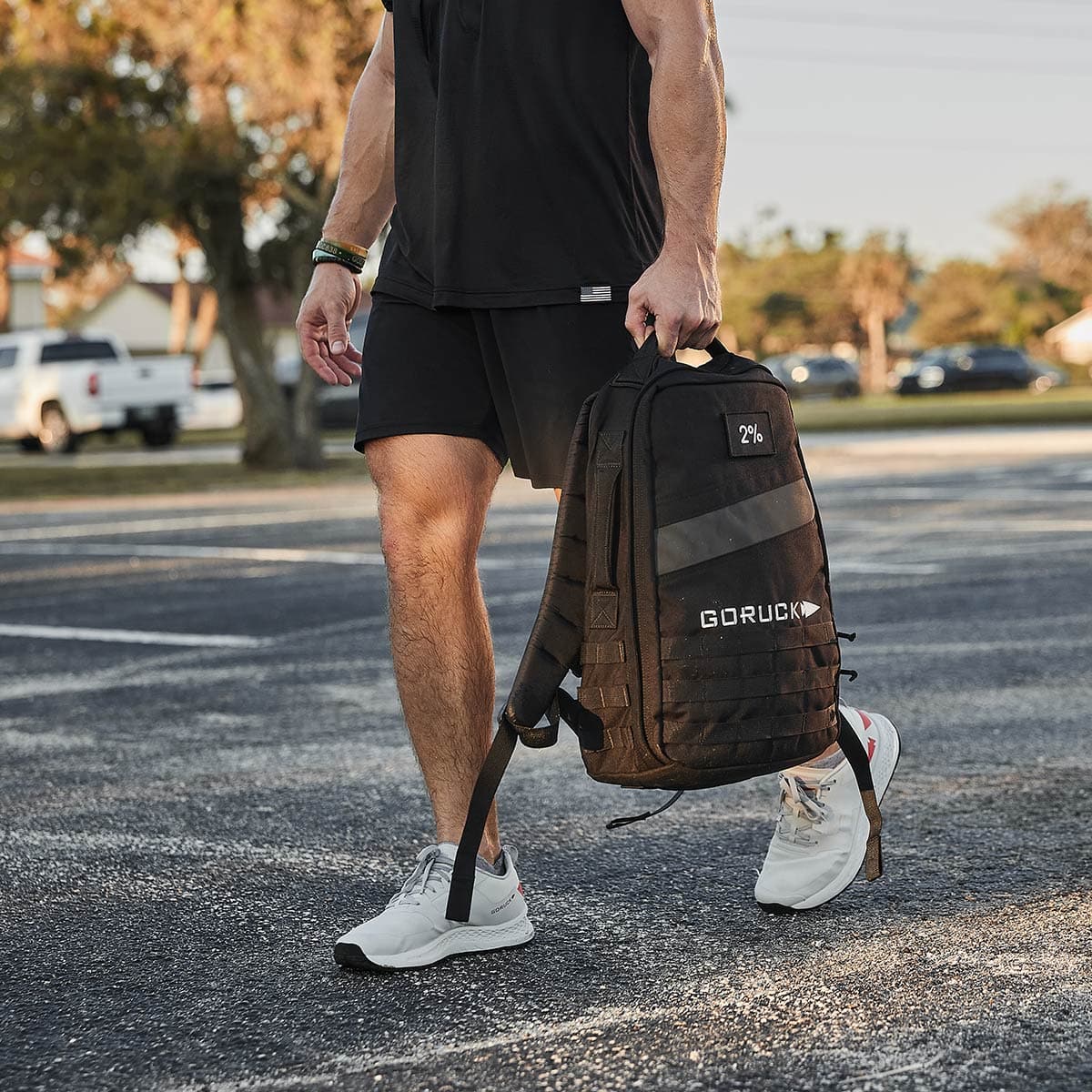 Man carrying a black GORUCK rucksack in outdoor setting, wearing athletic gear