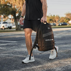 Man carrying a black GORUCK rucksack in outdoor setting, wearing athletic gear