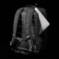 A GORUCK GR2 black backpack, designed to resemble Special Forces medical packs, reveals a laptop emerging from the back compartment against a dark background.