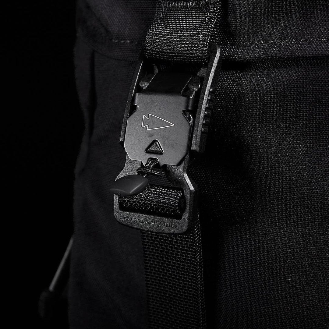 Close-up of a GORUCK M23 - Cordura backpack strap with a plastic buckle featuring an arrow design. Crafted from durable materials, this modern rucksack component stands out against the black background, highlighting the texture and details of the strap and buckle.