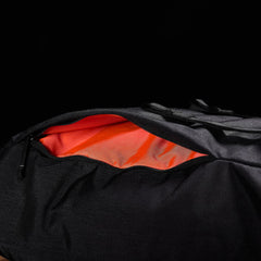 An M23 - Cordura rucksack by GORUCK, partially unzipped to reveal a bright orange interior lining against a dark background, showcasing its modern design and durable materials.