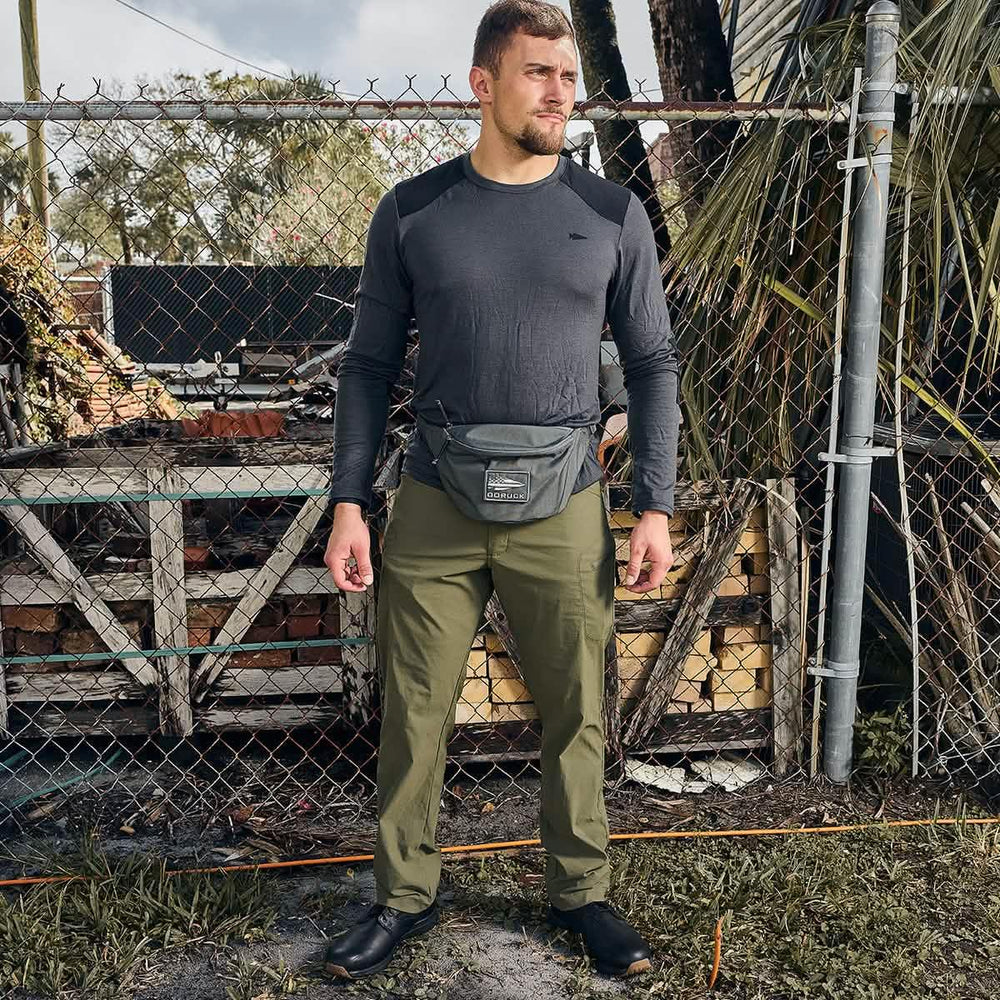 Man wearing GORUCK gear with a gray chest rig and olive pants outdoors by a fence
