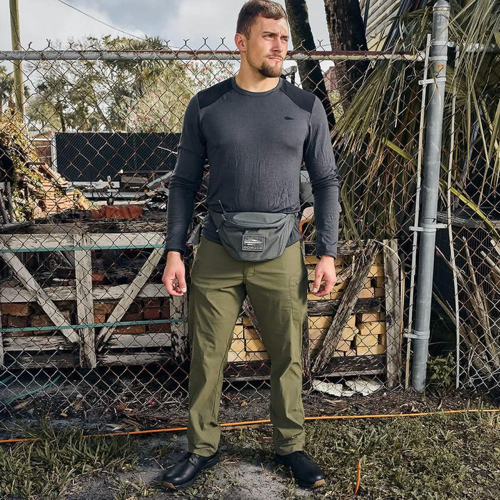 Man wearing GORUCK gear with a gray chest rig and olive pants outdoors by a fence