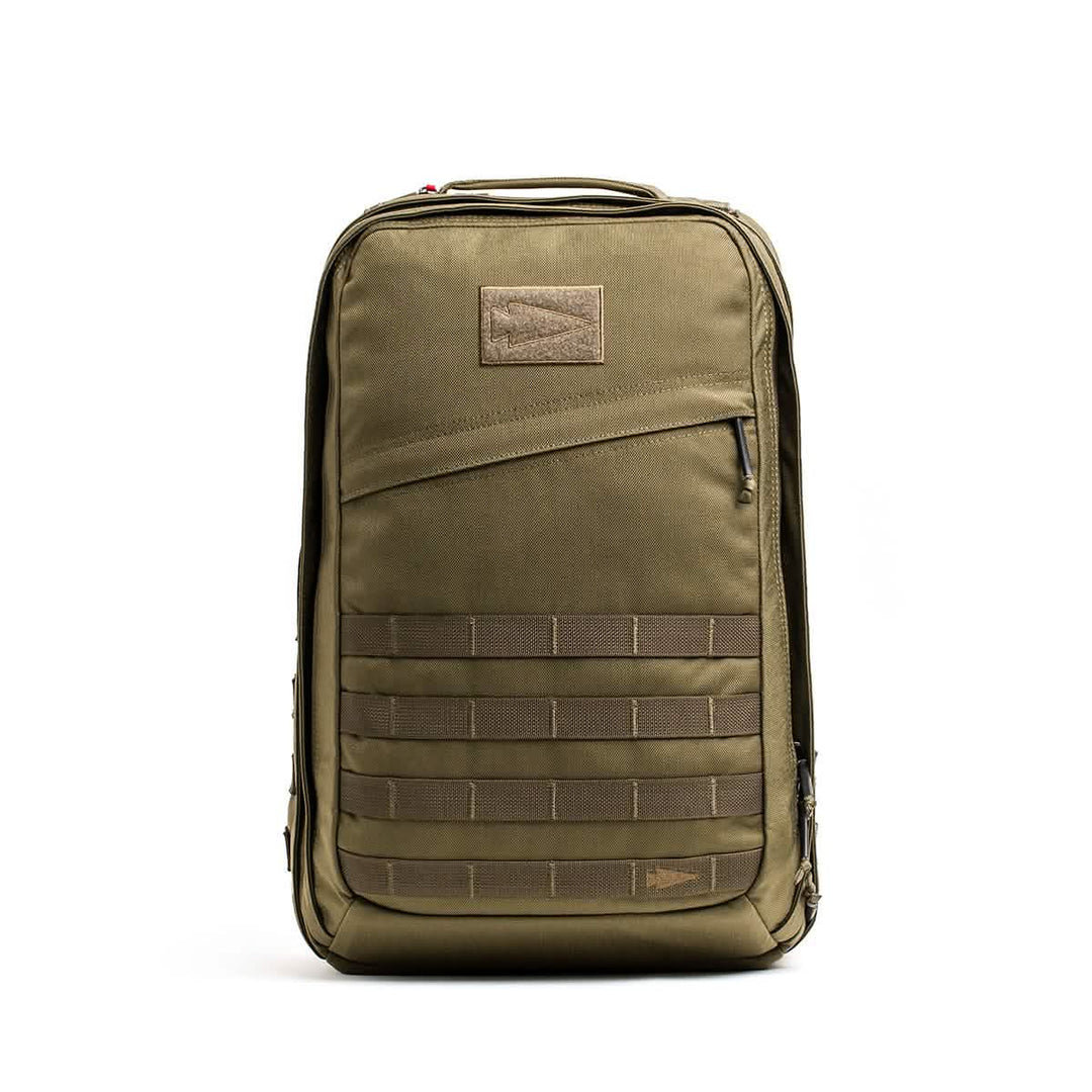 The GORUCK GR2 is an olive green Special Forces-inspired backpack with a front zipper pocket and horizontal webbing straps, standing upright; perfect as a carry-on compliant travel rucksack.