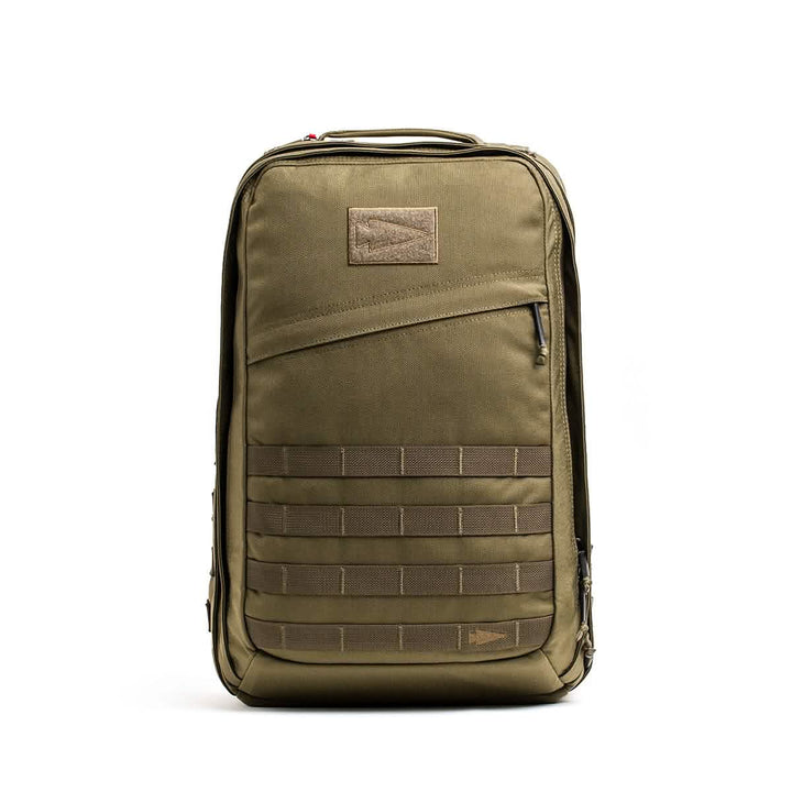 The GORUCK GR2 is an olive green Special Forces-inspired backpack with a front zipper pocket and horizontal webbing straps, standing upright; perfect as a carry-on compliant travel rucksack.