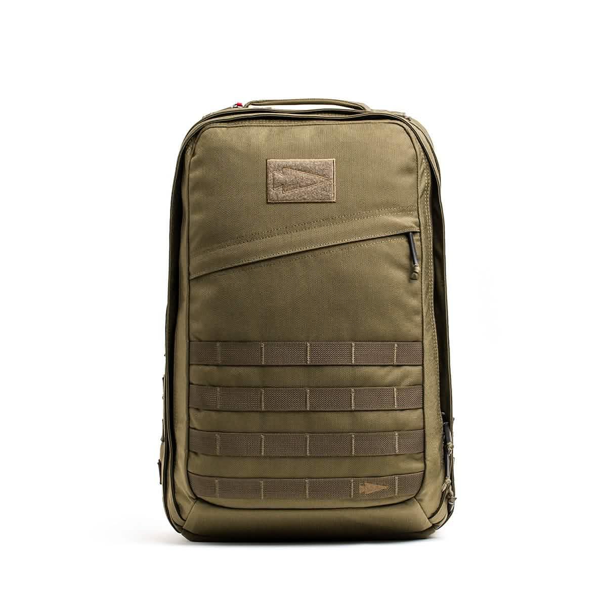 The GORUCK GR2 olive green tactical carry-on rucksack features a front zipper pocket and MOLLE webbing, shown standing upright against a white background.
