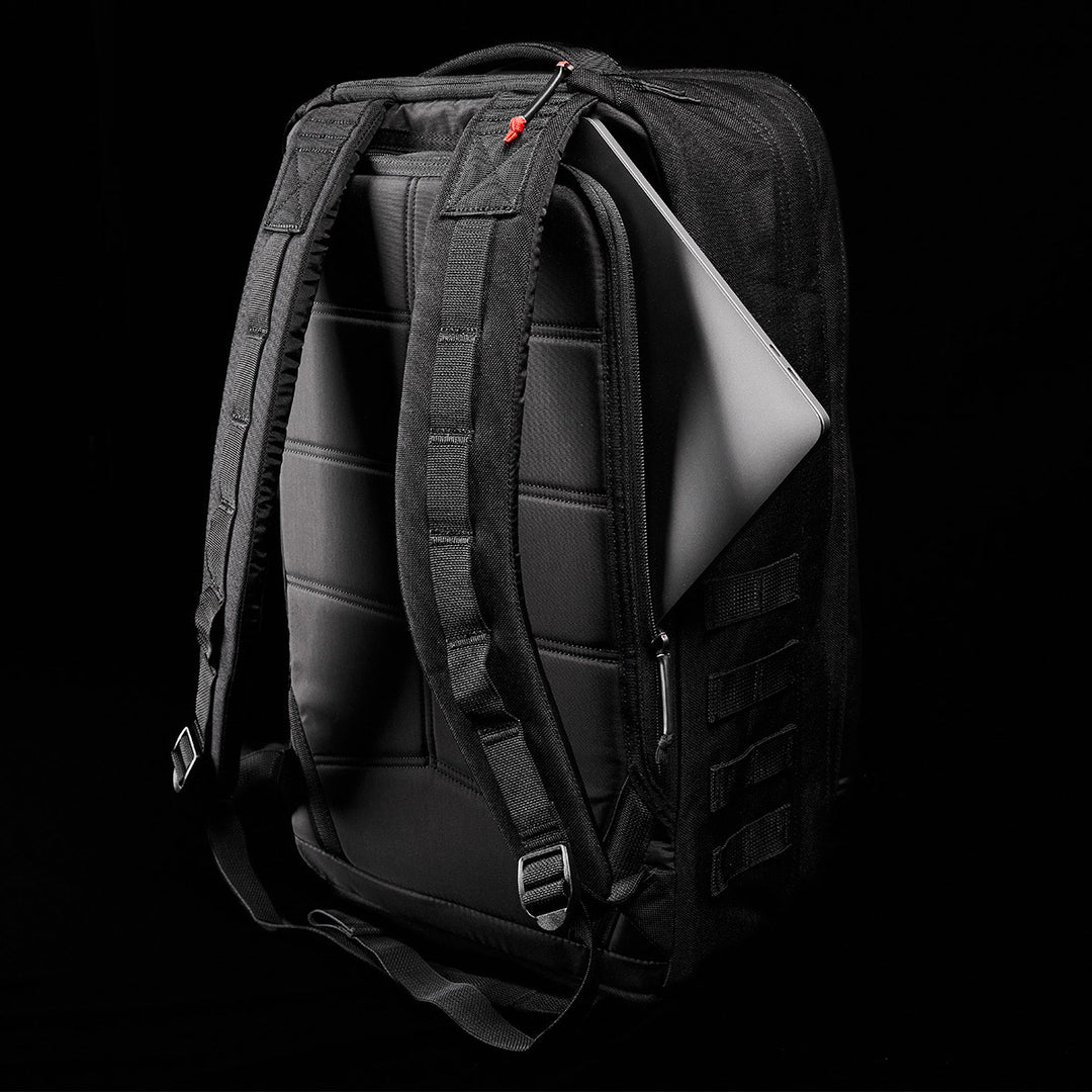 The GORUCK GR2 black backpack, evoking the rugged style of Special Forces medical packs, features padded straps and is slightly open to show a laptop inside against a dark background. It comes with the added assurance of a Scars Lifetime Guarantee for peace of mind.
