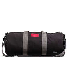 Introducing the GORUCK Gym Bag - Cordura, a sleek 38L bag crafted from durable CORDURA fabric, featuring gray straps and a distinct red label on the side.