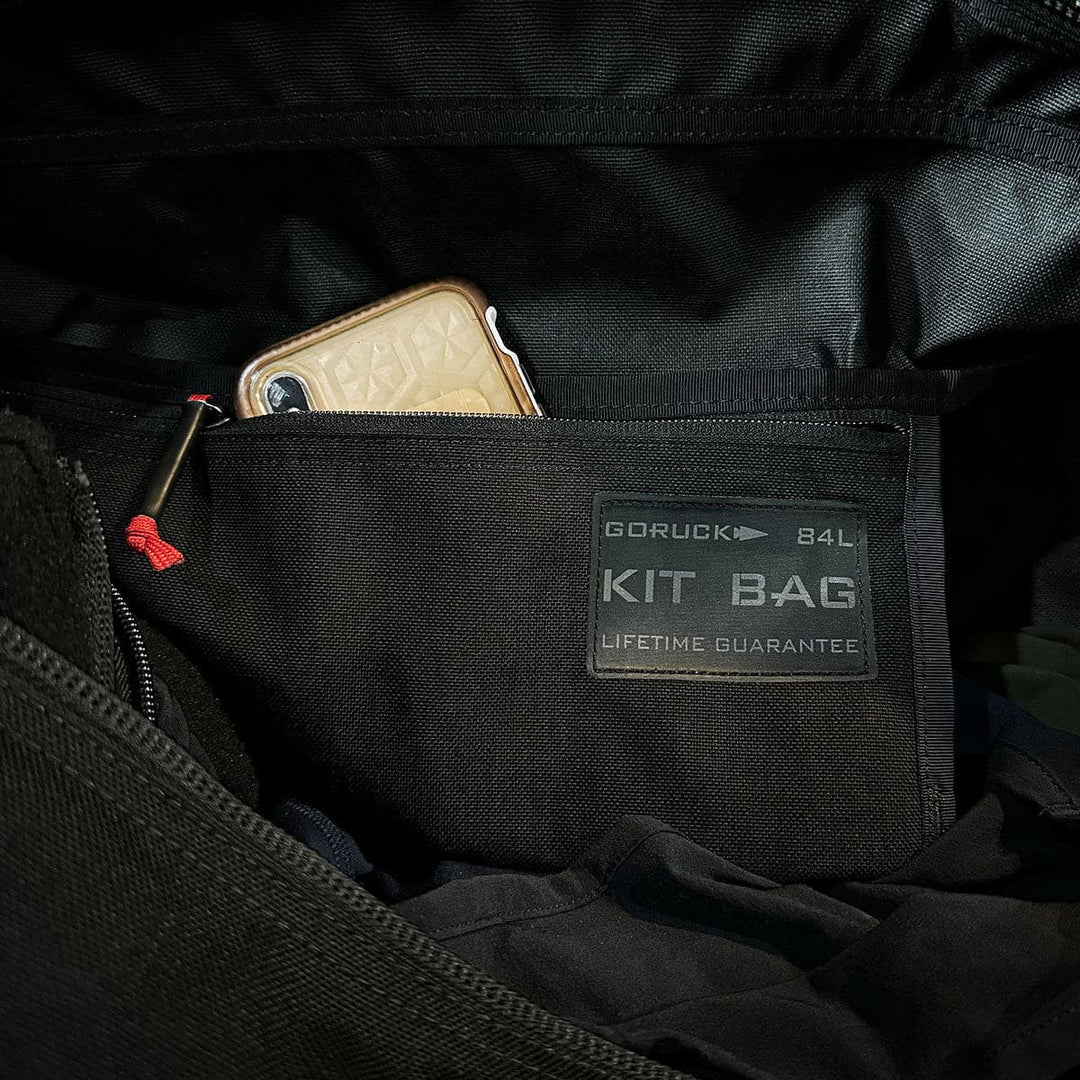 Unzip the black GORUCK Kit Bag - 84L, revealing a phone neatly placed in the pocket.
