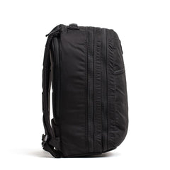 A side view of the GORUCK Bullet Ruck Double Compartment, made from ripstop nylon, showcasing its sleek black design with dual zippered compartments and adjustable shoulder straps.