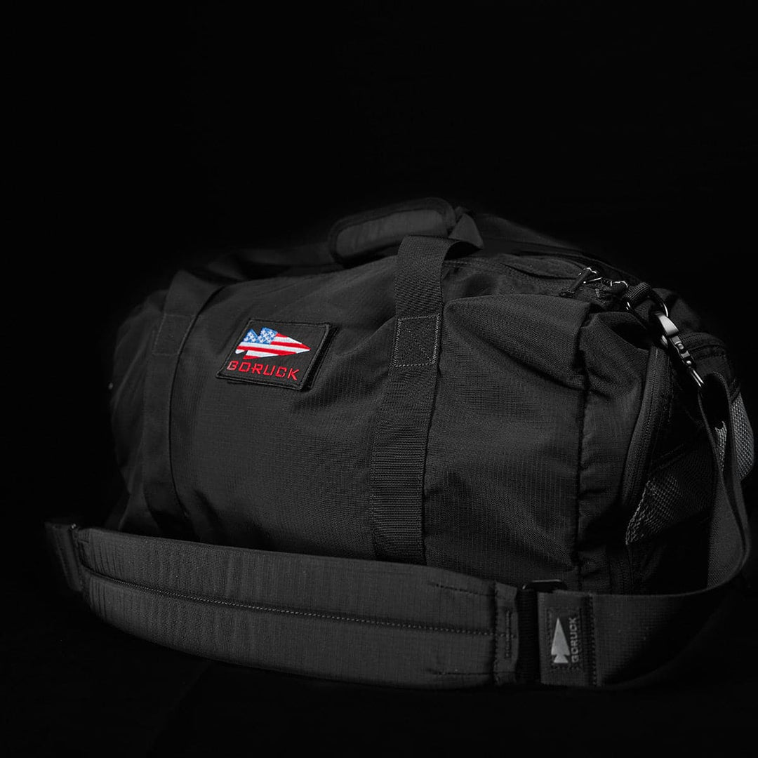 The Gym Bag - Ripstop ROBIC® by GORUCK is designed in black from durable ripstop nylon and includes a shoulder strap and a flag patch on its dark fabric. Perfect for gym use, it has a handy shoe compartment to keep your essentials organized.