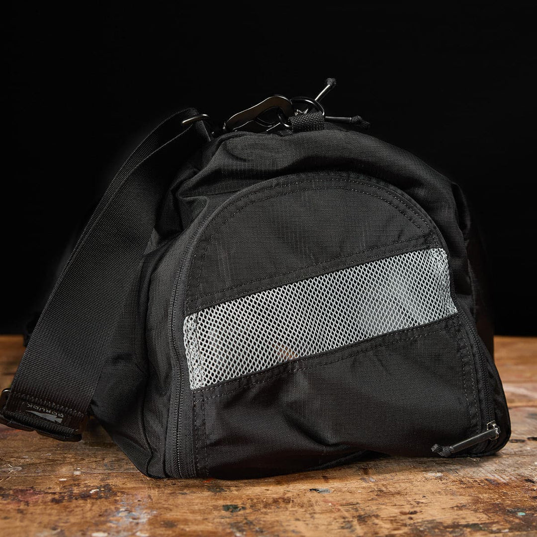 Gym Bag - Ripstop ROBIC® by GORUCK in black, made from durable ripstop fabric with a mesh pocket, displayed on a wooden surface with a dark background.