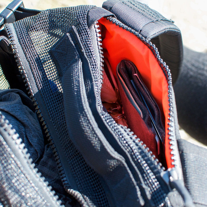 The Mesh Ruck is open to reveal its orange lining, displaying a wallet and phone inside the main compartment.