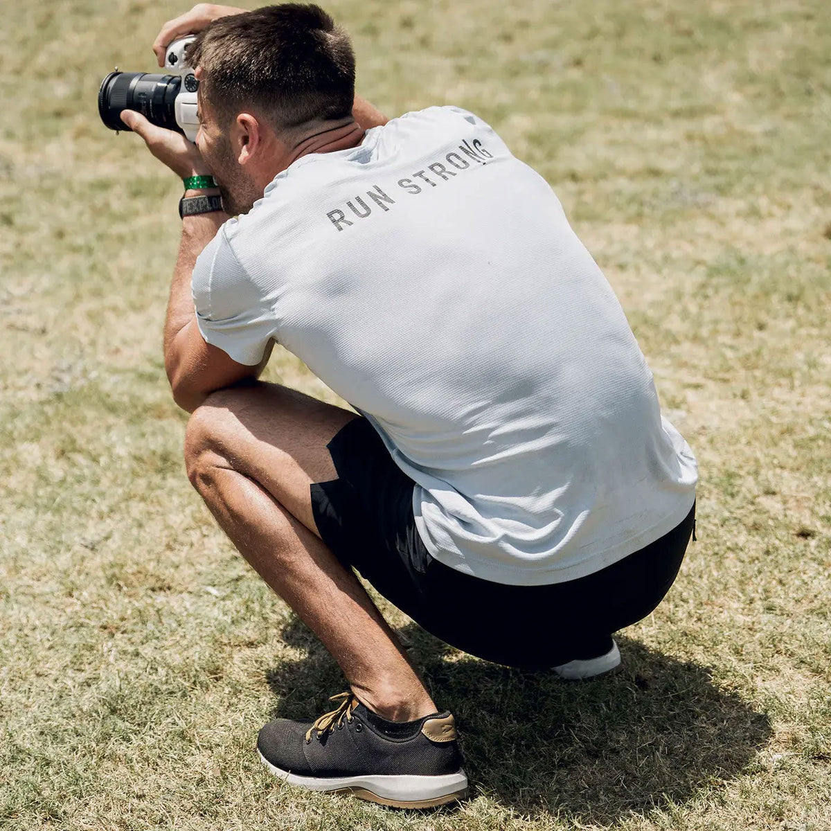 A man kneeling on grass with a camera.