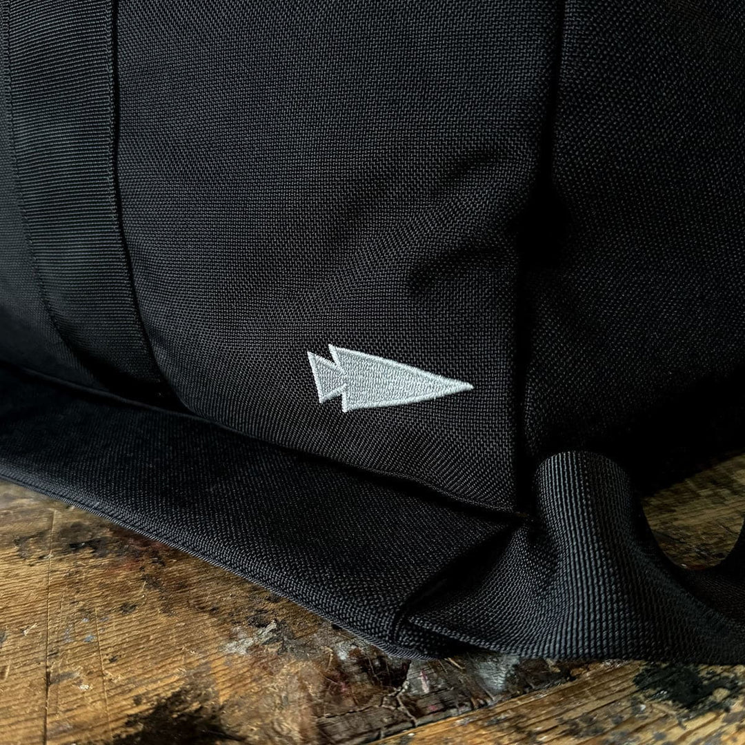 A Kit Bag - 84L from GORUCK, made of fabric and featuring a white arrowhead logo, sits on a wooden surface.
