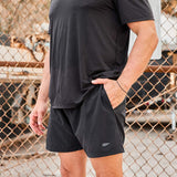Man wearing GORUCK black athletic shorts and t-shirt outdoors near chain-link fence