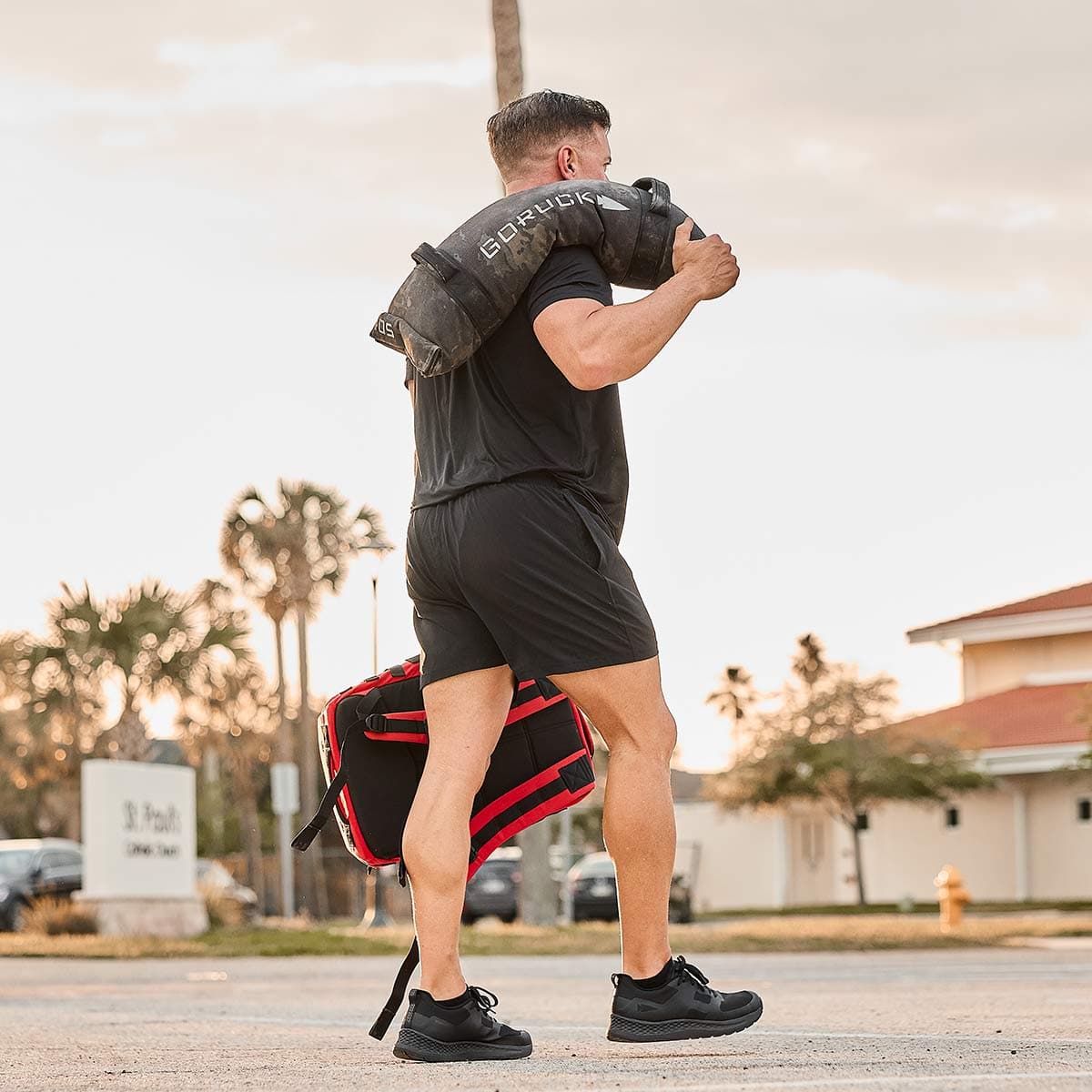 Man outdoors carrying GORUCK sandbag and rucksack, showcasing rucking fitness gear