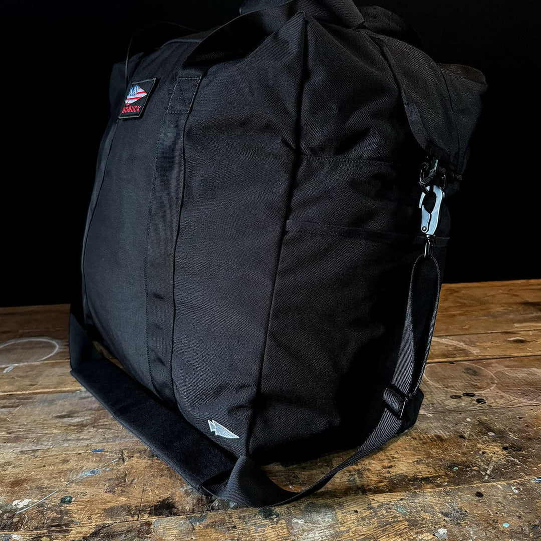 A GORUCK Kit Bag - 84L (Includes Shoulder Strap) in black is elegantly situated on a wooden surface.