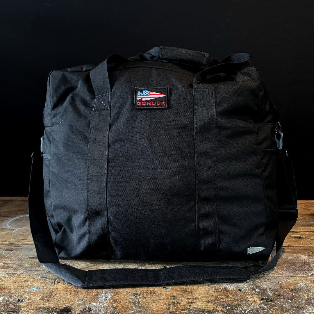The GORUCK Kit Bag - 84L, featuring an American flag patch, rests on a wooden surface, evocative of a Special Forces Flight Bag.