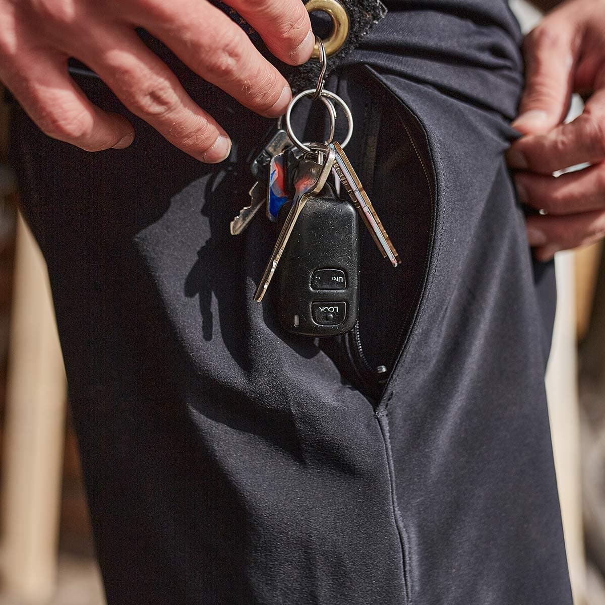 Close-up of keys and key fob in zippered pocket of black GORUCK pants, outdoor setting