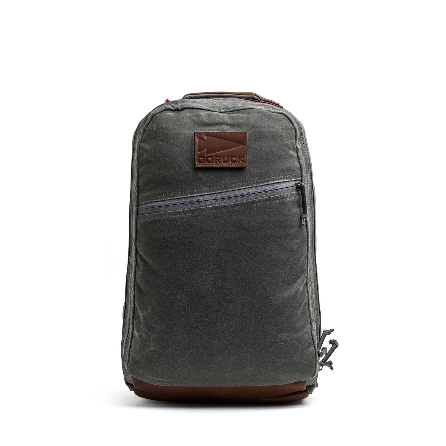 The GORUCK Bullet Ruck - Heritage Waxed Canvas - 18L is a gray waxed canvas backpack featuring a brown leather patch, front zipper pocket, and top handle. Shown on a white background, it’s designed as the perfect travel daypack for your daily adventures.
