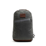 The GORUCK Bullet Ruck - Heritage Waxed Canvas - 18L is a gray waxed canvas backpack featuring a brown leather patch, front zipper pocket, and top handle. Shown on a white background, it’s designed as the perfect travel daypack for your daily adventures.