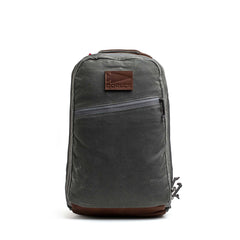 The GORUCK Bullet Ruck - Heritage Waxed Canvas - 18L is a gray waxed canvas backpack featuring a brown leather patch, front zipper pocket, and top handle. Shown on a white background, it’s designed as the perfect travel daypack for your daily adventures.