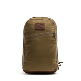 The GORUCK Bullet Ruck - Heritage Waxed Canvas - 18L is a brown backpack crafted from durable waxed canvas, featuring a front zipper pocket and a leather patch logo on the upper front—ideal for use as a travel daypack.