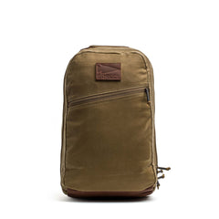 The GORUCK Bullet Ruck - Heritage Waxed Canvas - 18L is a brown backpack crafted from durable waxed canvas, featuring a front zipper pocket and a leather patch logo on the upper front—ideal for use as a travel daypack.