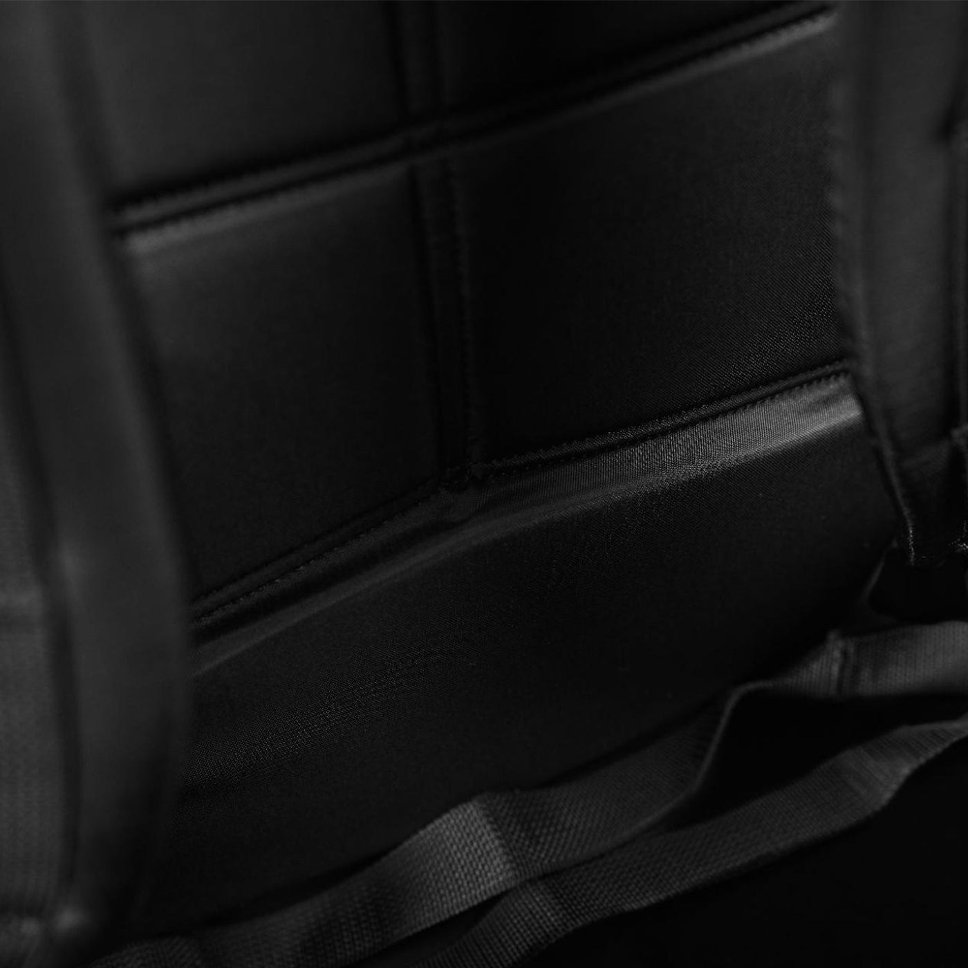 Close-up of black padded fabric with visible stitching and seams, possibly part of a backpack or seat.