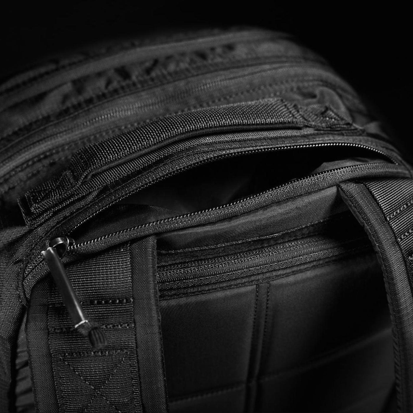 Close-up of a black backpack with a partially open zipper and visible textured stitching.