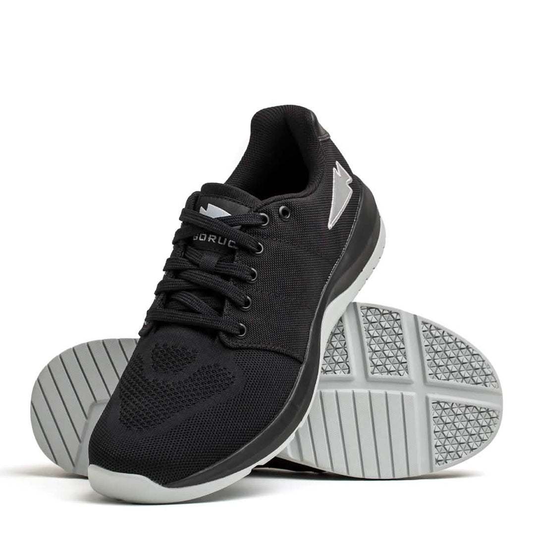The GORUCK Ballistic Trainers in Black + Glacier Grey W / Silver Reflective Spearhead feature durable CORDURA® Ballistic Nylon and white soles—one shoe upright, one on its side—for lasting fitness performance.