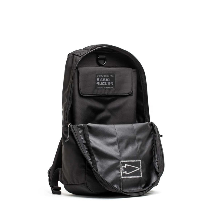 Black Basic Rucker® backpack with an open front pocket, displaying a patch labeled "Basic Rucker®" and a stitched arrow design.