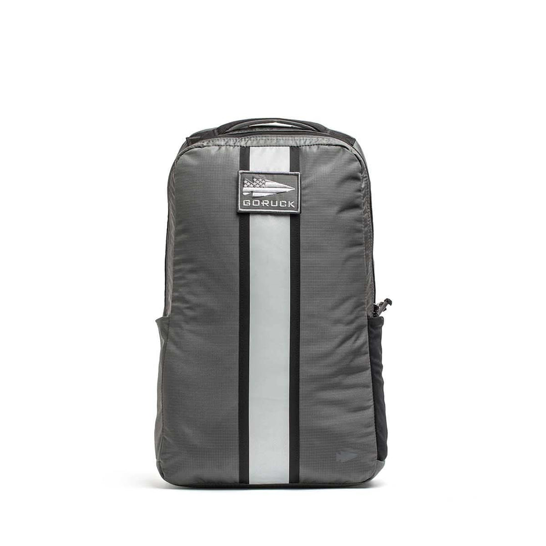 A gray Basic Rucker® backpack with a vertical reflective stripe and front patch, designed for weighted rucking, shown on a white background.