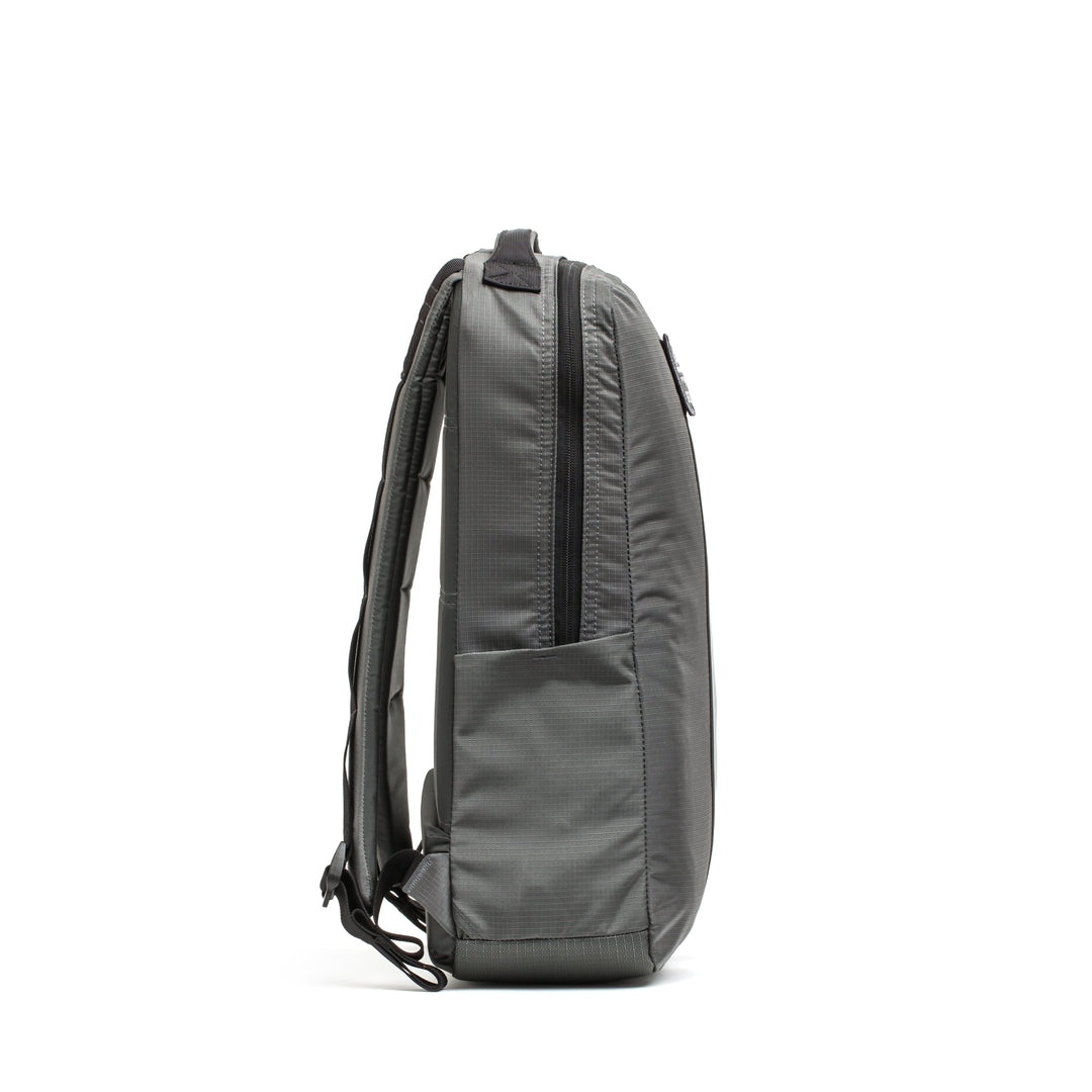 The Basic Rucker® in gray is shown from the side, featuring padded straps and a front zip pocket for convenient storage.