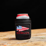 A cold beer rests on a wooden surface in a black GORUCK Ballistic Beer Jacket featuring an American flag arrow patch.