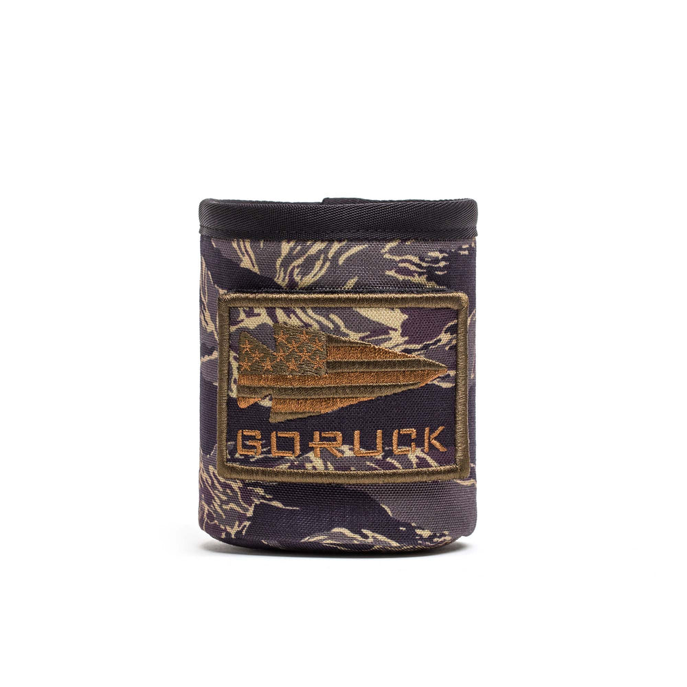 The Ballistic Beer Jacket by GORUCK is a camo-patterned koozie, crafted from durable 1000D CORDURA, featuring an American flag spear patch and "GORUCK" on the front—perfect protection for your drink.