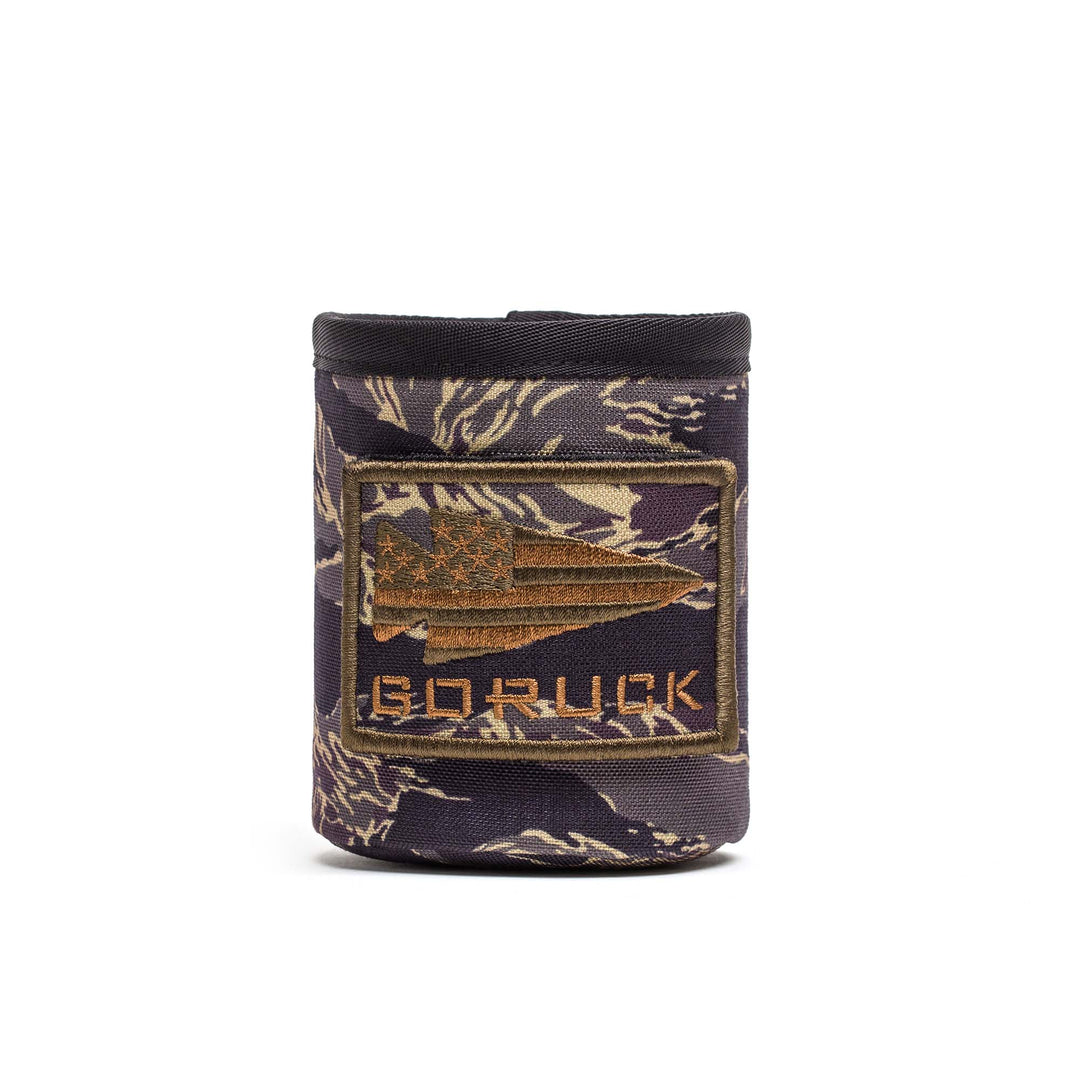 The Ballistic Beer Jacket by GORUCK is a camo-patterned koozie, crafted from durable 1000D CORDURA, featuring an American flag spear patch and "GORUCK" on the front—perfect protection for your drink.