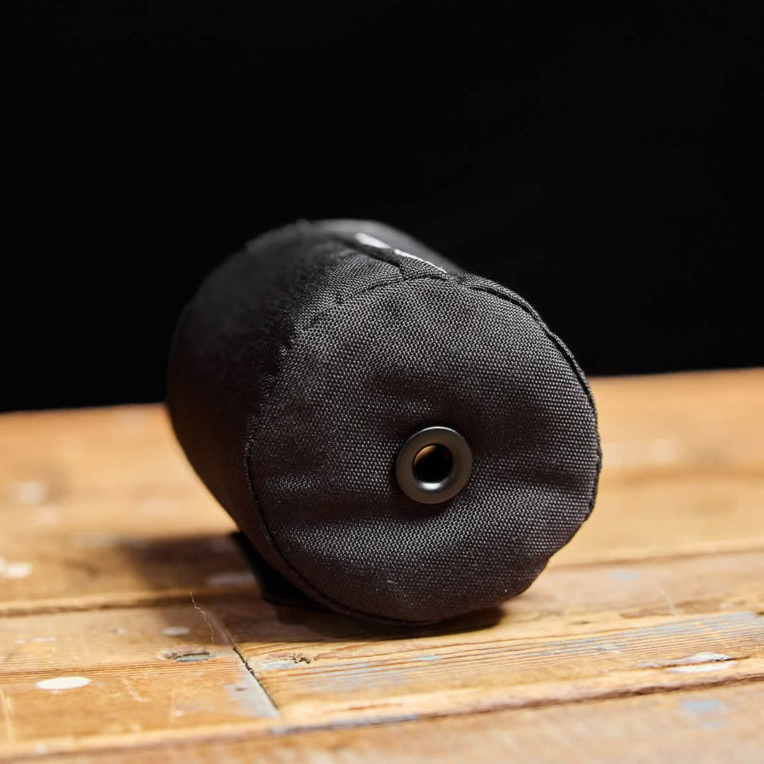 A close-up of the GORUCK Ballistic Beer Jacket, made from black 1000D CORDURA with a metal grommet, resting on wood—durable gear for keeping your beer cold.