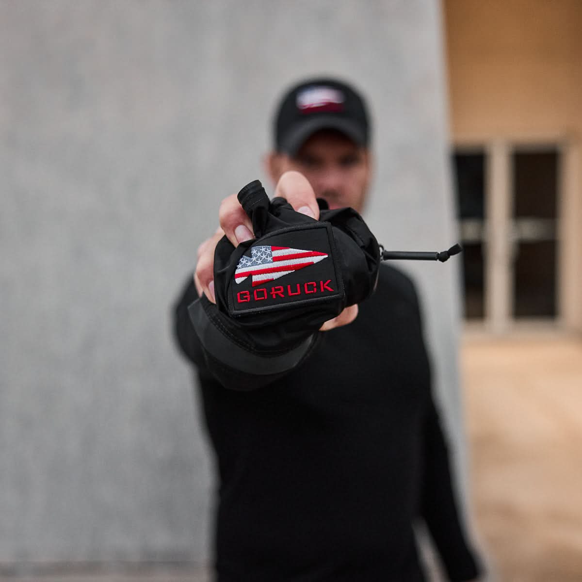 Man holding compact black GORUCK packable gear with American flag patch outdoors