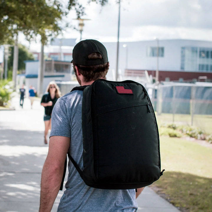 Man wearing GORUCK backpack with American flag patch outdoors on a sunny day
