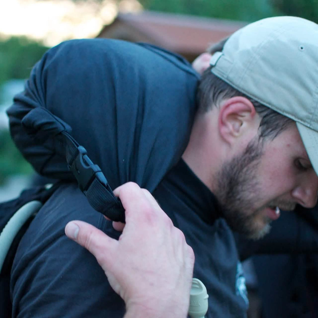 A man in a cap adjusts the strap of his GORUCK Brick Bag (5-50 LBS) on his shoulder while outdoors.