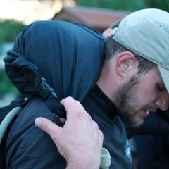 A man in a cap adjusts the strap of his GORUCK Brick Bag (5-50 LBS) on his shoulder while outdoors.