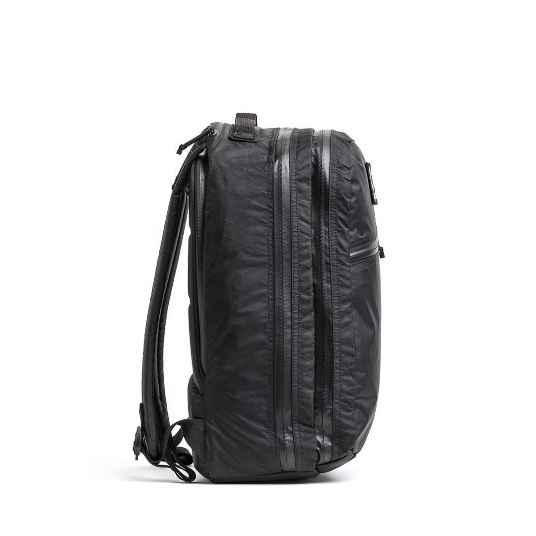 The Double Compartment Bullet Ruck - XPAC, shown upright from the side, features visible zippers, padded shoulder straps, and an ultra-durable laptop compartment.