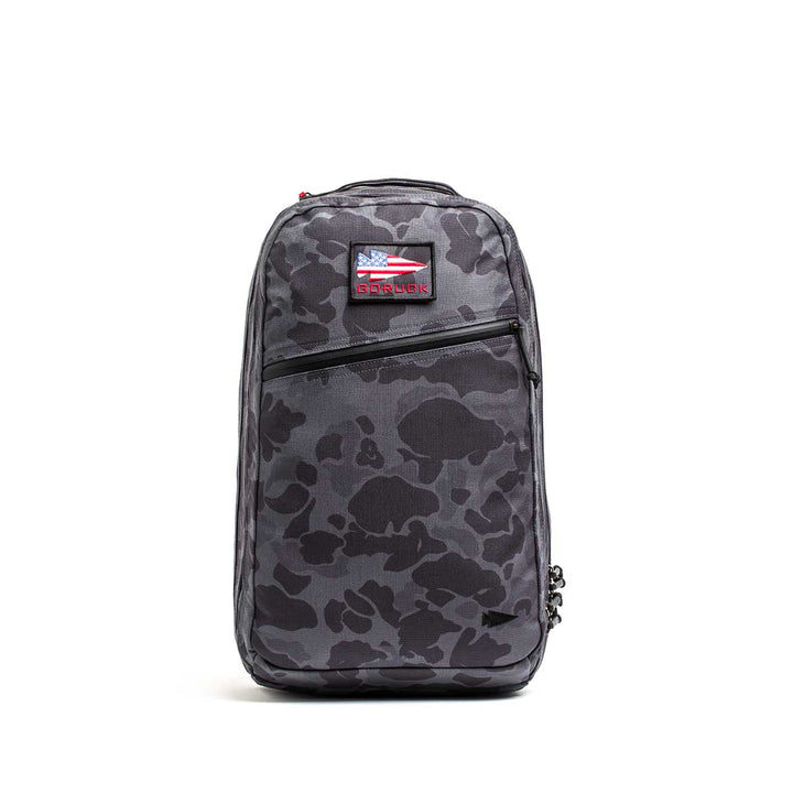 The Double Compartment Bullet Ruck - Ballistic Nylon Cordura - 18L is a gray camo travel backpack with a front zipper pocket, bombproof laptop compartment, and a small USA flag patch near the top.
