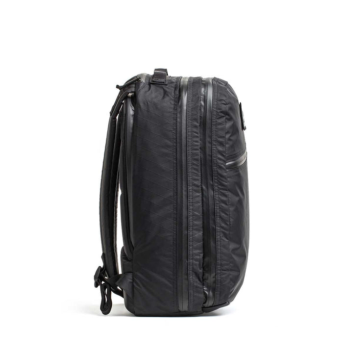 The Double Compartment Bullet Ruck - XPAC, shown from the side against a white background, is a black travel backpack featuring side zippers and an ultra-durable laptop compartment.