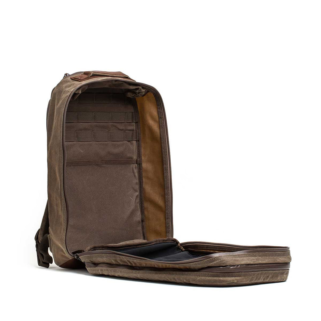 The GORUCK Bullet Ruck - Heritage Waxed Canvas - 18L backpack is shown unzipped with interior pockets and compartments visible against a white background—perfect for hands-free travel convenience.